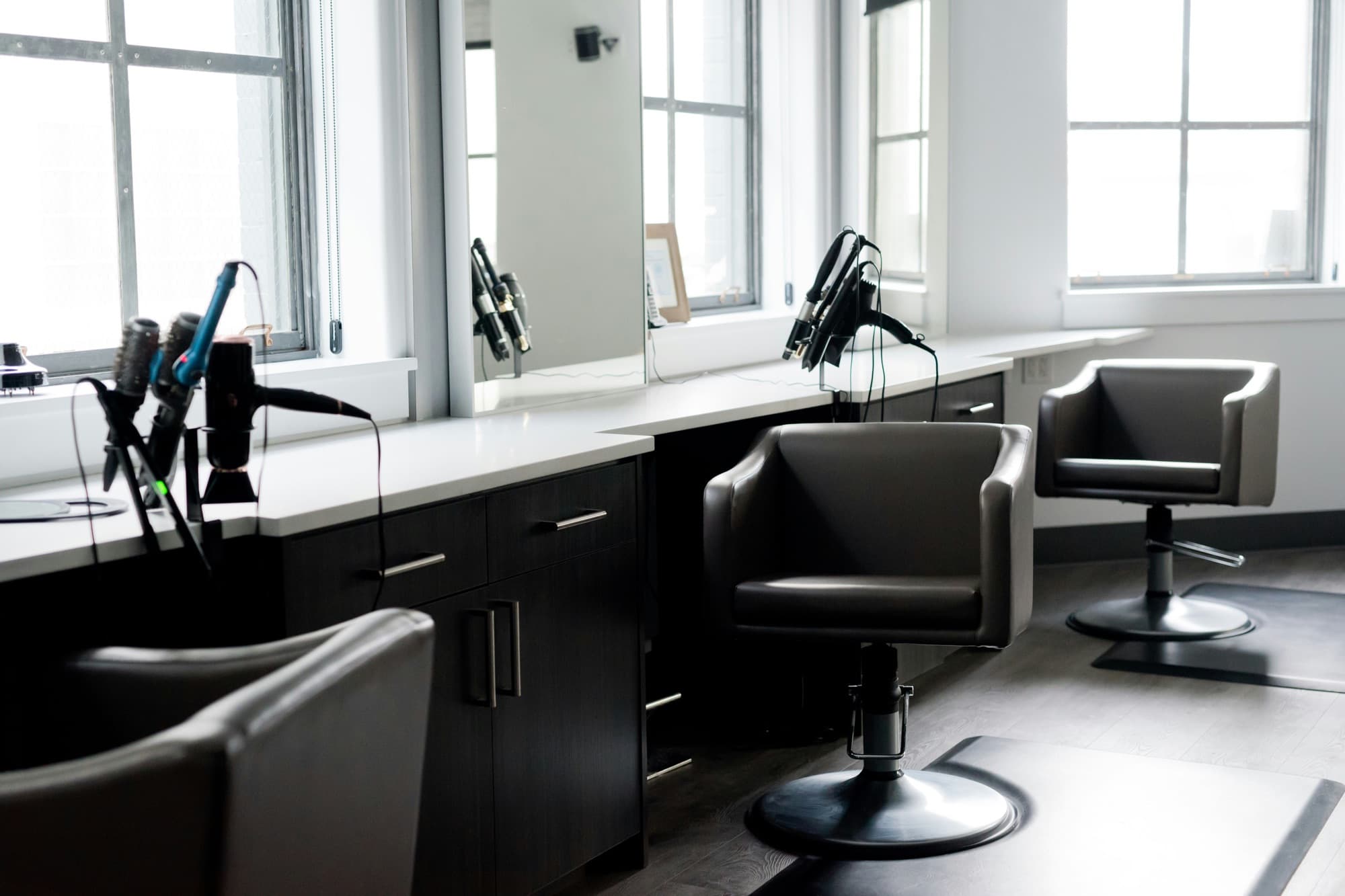 Hair salon styling stations with chairs, mirrors and hair tools beside large windows